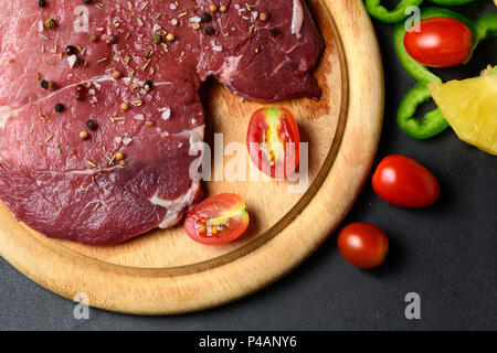 Fresh raw beef steak with dry rosemary leaf and pepper on black table background, Marinated meat for barbecue Stock Photo