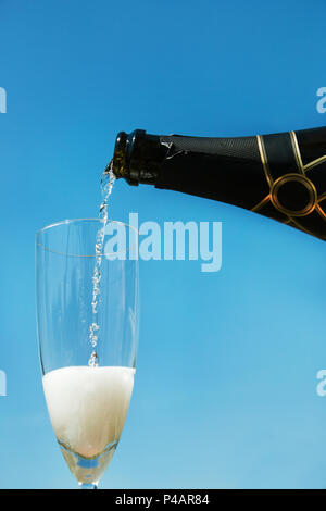 Pouring champagne into the glass against blue sky background. Stock Photo