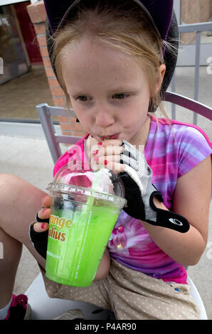 Girl age 7 wearing a bicycle helmet enjoying a rest break in an outdoor cafe drinking her green slushie. Minneapolis Minnesota MN USA Stock Photo