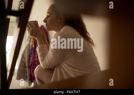 Woman having coffee while relaxing on stairs at home Stock Photo