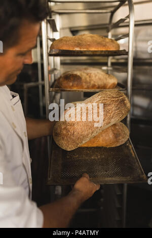 Male baker checking baked bread Stock Photo