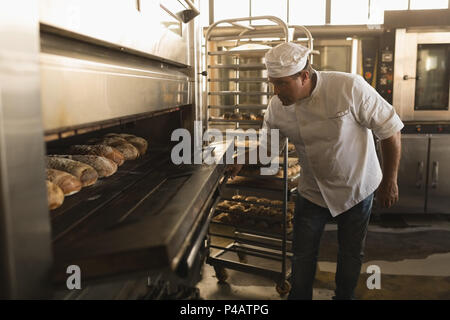 Male baker using baking owen in bakery shop Stock Photo