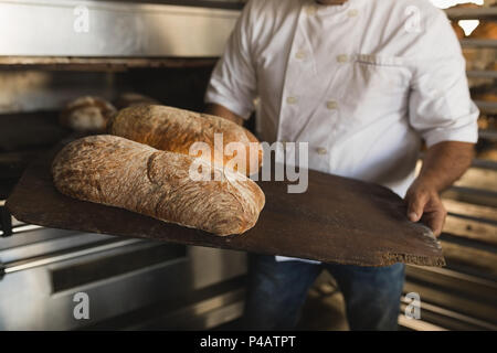 Male baker holding baked bread in bakery shop Stock Photo