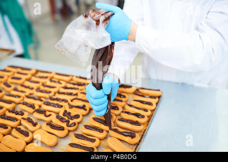 Confectionery factory employee filling pastry with chocolate cream Stock Photo