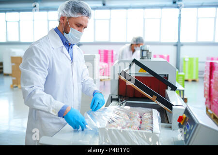 Confectionery factory employee wrapping box into packaging film Stock Photo