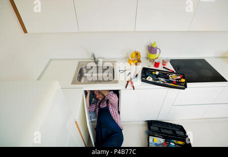 Worker repairs the leakage problem in the kitchen sink Stock Photo