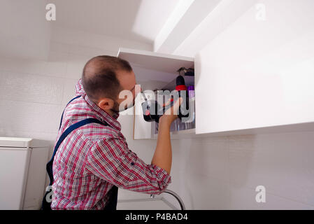 Handyman fixing the kitchen cabinet doors with battery drill Stock Photo