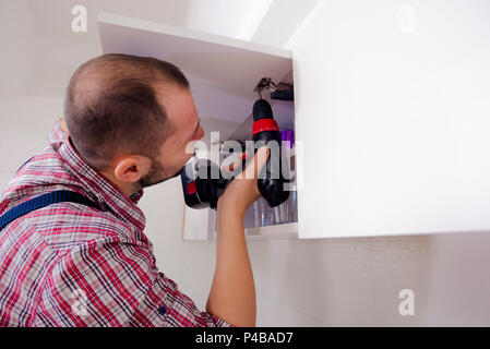 Handyman fixing the kitchen cabinet doors with battery drill Stock Photo