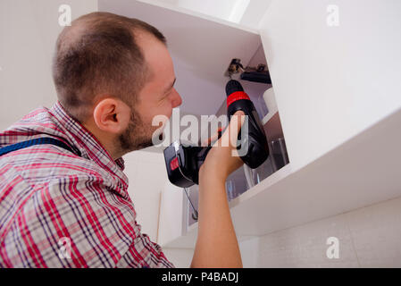 Handyman fixing the kitchen cabinet doors with battery drill Stock Photo