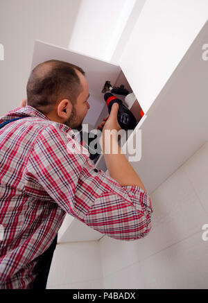 Handyman fixing the kitchen cabinet doors with battery drill Stock Photo
