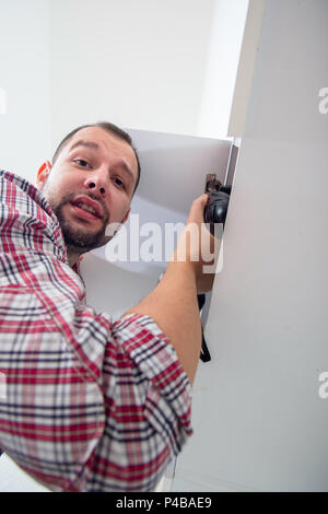 Handyman fixing the kitchen cabinet doors with battery drill Stock Photo