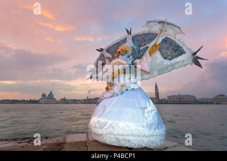 Typical mask of Carnival of Venice at San Giorgio island with Church of Santa Maria della Salute and San Marco Bell Tower on background, Venice, Veneto, Italy Stock Photo