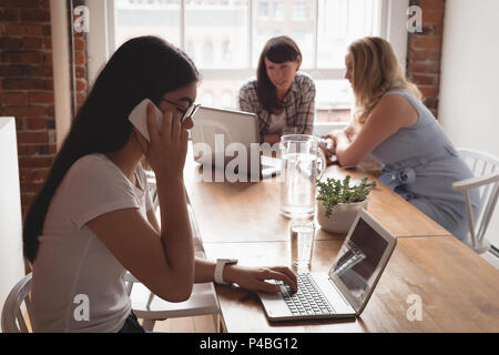 Executive talking on mobile phone while using laptop Stock Photo