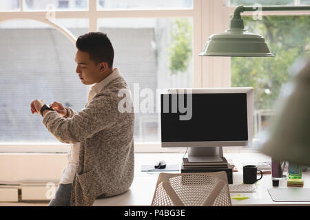 Executive sitting on desk checking time in his smartwatch Stock Photo