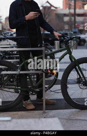Man standing next to his bike and using mobile phone Stock Photo
