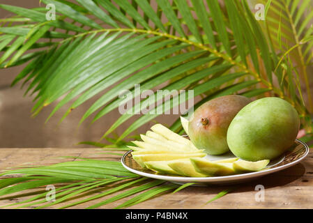 Mango fruit on plate sliced with sunny green natural background Stock Photo