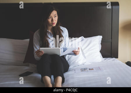 Businesswoman holding documents while using digital tablet on bed Stock Photo