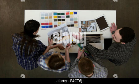 Four designers discussing layouts and color samples at office desk Stock Photo