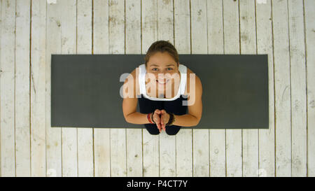 Happy mature woman doing yoga with namaste gesture looking at camera smiling Stock Photo