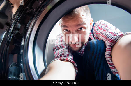 Repair man fixing the washing machine in the bathroom, view from inside the machine Stock Photo