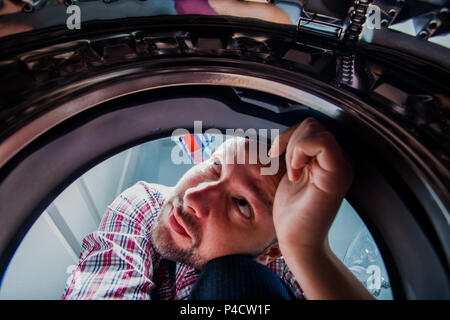Repair man fixing the washing machine in the bathroom, view from inside the machine Stock Photo