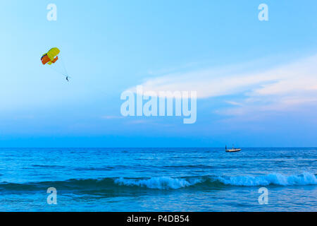 Colorful parasail wing pulled by boat in the sea water, on blue sky background. Stock Photo