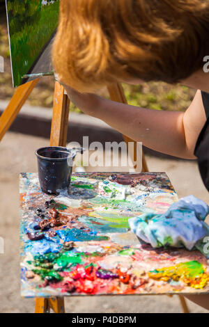 A close-up artist paints on a canvas an urban landscape of a summer embankment with atractions of oil paints Stock Photo