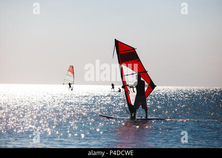 Windsurfers in the sea during sunset, active lifestyle Stock Photo