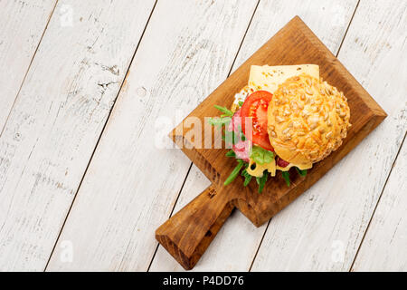Tasty appetizer of thinly sliced spicy salami on bread with cheese, tomato and herbs on a cutting board with copy space. Stock Photo