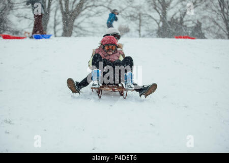 Two little girls are going down a big hill on a sled together in the snow. Stock Photo