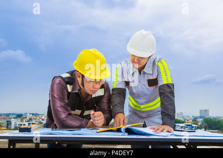 Asian construction engineer and his foreman working together looking at the blueprint at construction site, good for teamwork and engineering theme Stock Photo