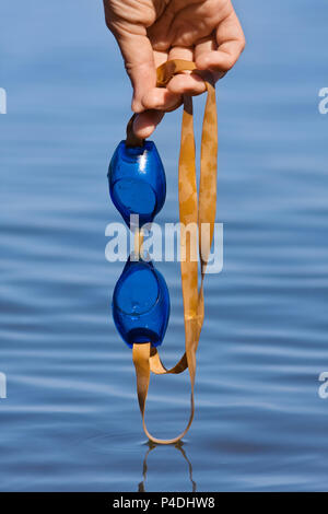 hand of smimmer with swimming goggles on blue blurred background Stock Photo