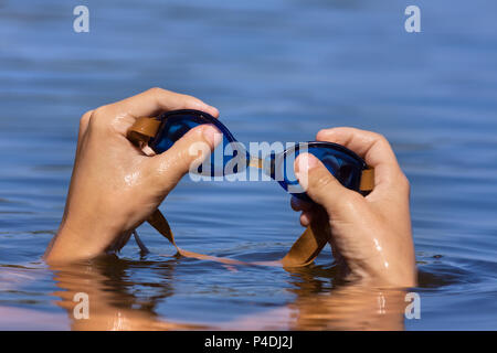 hand of smimmer holding swimming goggles on water background Stock Photo