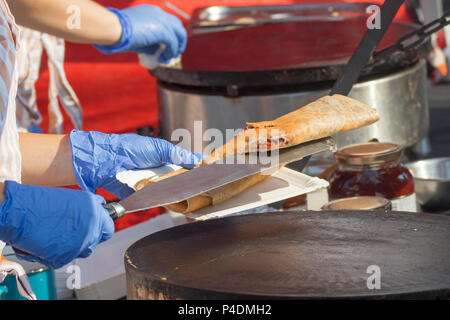 Farmers creperie, farmers street food market, vendor performs how to make pancakes - crepes. Chef's hands in blue gloves serve a chopped pancake on a  Stock Photo