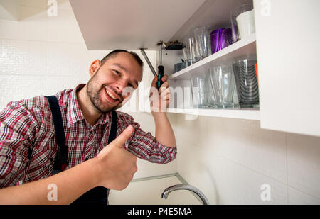 Handsome guy repair door on the cabinet in the kitchen Stock Photo