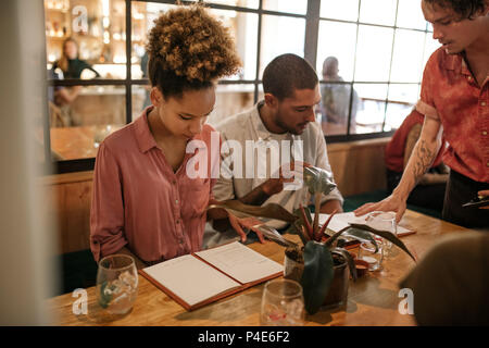 Group of young friends reading menus at a restaurant table Stock Photo