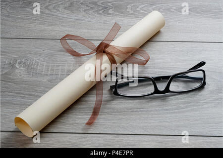 a diploma rolled up and tied with a red ribbon on the table with a pair of glasses Stock Photo