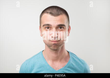 Humorous emotional portrait of grimacing young man. He is blowing his cheeks. He is trying not to laugh Stock Photo