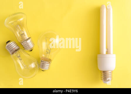 Energy-saving Lamp vs. incandescent lamps. The concept of energy saving . On a yellow background.One energy-saving bulb corresponds to three incandesc Stock Photo