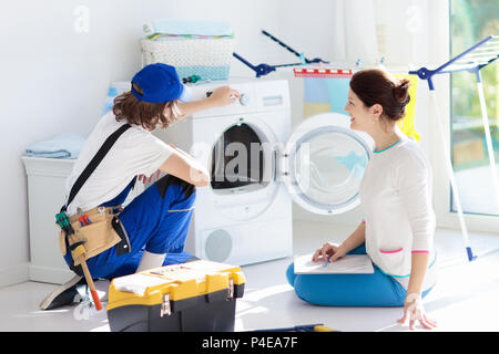 Washing machine repair service. Young technician examining and repairing tumble dryer. Woman looking at broken household appliance. Plumber with custo Stock Photo