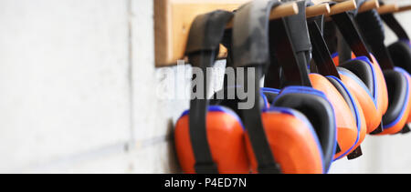 row of orange ear muffs ear protection on a rack. workplace health and  safety deafness concept. safe work practice Stock Photo - Alamy