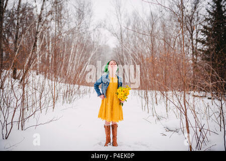 Girl standing in the snow holding a bunch of flowers Stock Photo