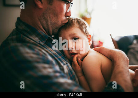Father sitting on couch cuddling his son and kissing him on the head Stock Photo