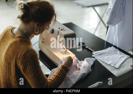 seamstress at work. woman working on a sewing machine, sitting at a table, sewing clothes, cloth Stock Photo