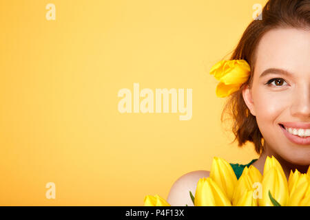 partial view of smiling woman with bouquet of yellow tulips isolated on orange Stock Photo