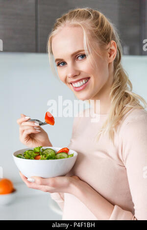 beautiful young blonde woman eating fresh healthy vegetable salad and smiling at camera Stock Photo