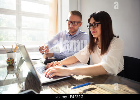 Two Happy Businesspeople Using Laptop At Workplace Stock Photo