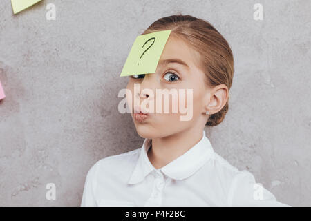 portrait of little girl with sticky note with question mark on face isolated on grey Stock Photo