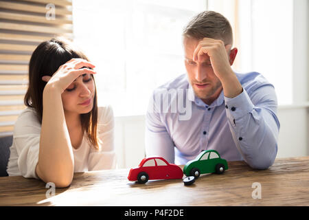 Upset Young Couple Looking At Red And Green Colored Car Crash Over Wooden Desk Stock Photo