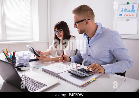 Two Young Businesspeople Calculating Invoice With Calculator Stock Photo